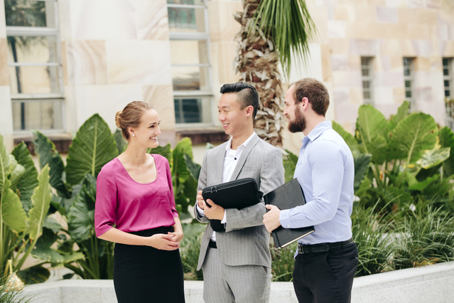 Image of three staff members standing around talking and smiling in front of the UQ sandstone 