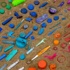 Image of different coloured plastics washed up on the sand.